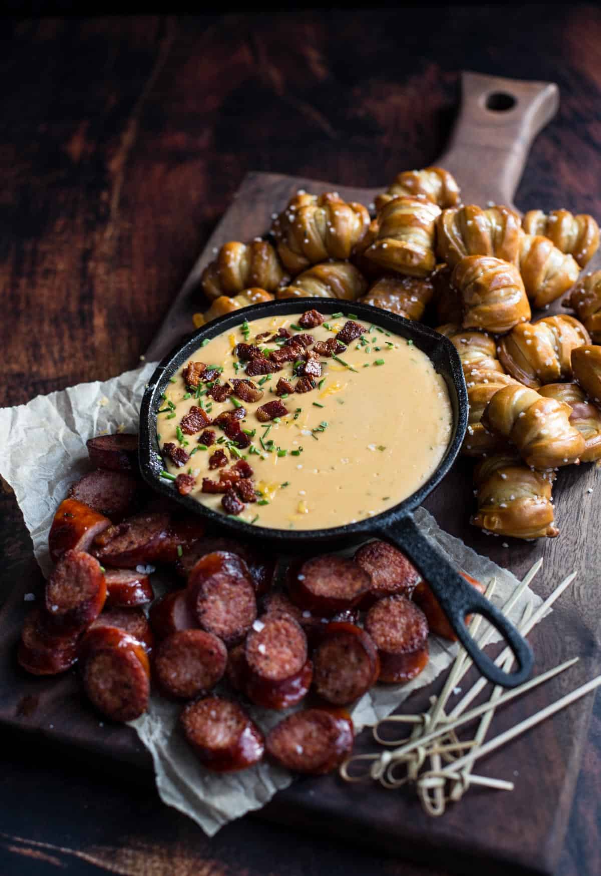 A platter with beer cheese dip and dipping options of soft pretzel bites and sausages