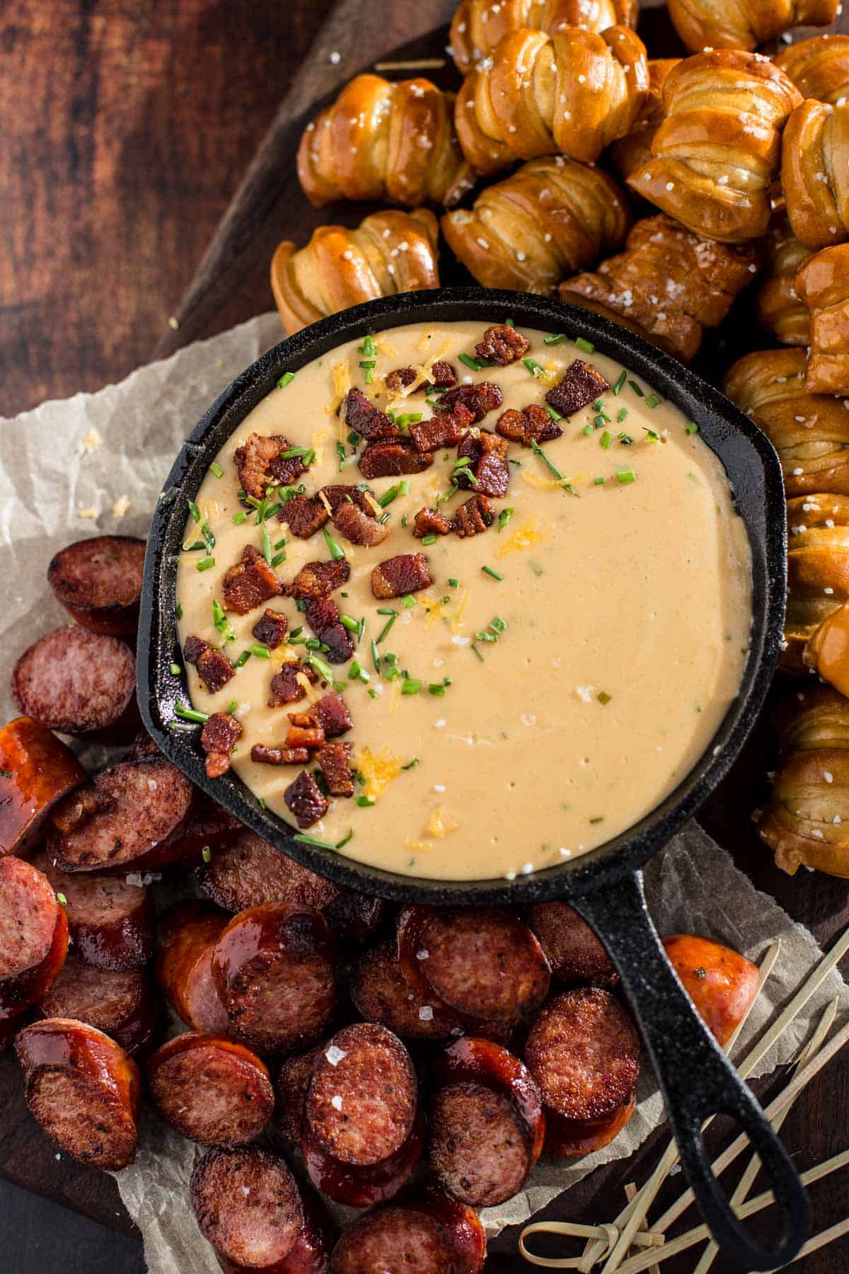 Beer Cheese Dip in cast iron pan on plate with pretzels and sausage.
