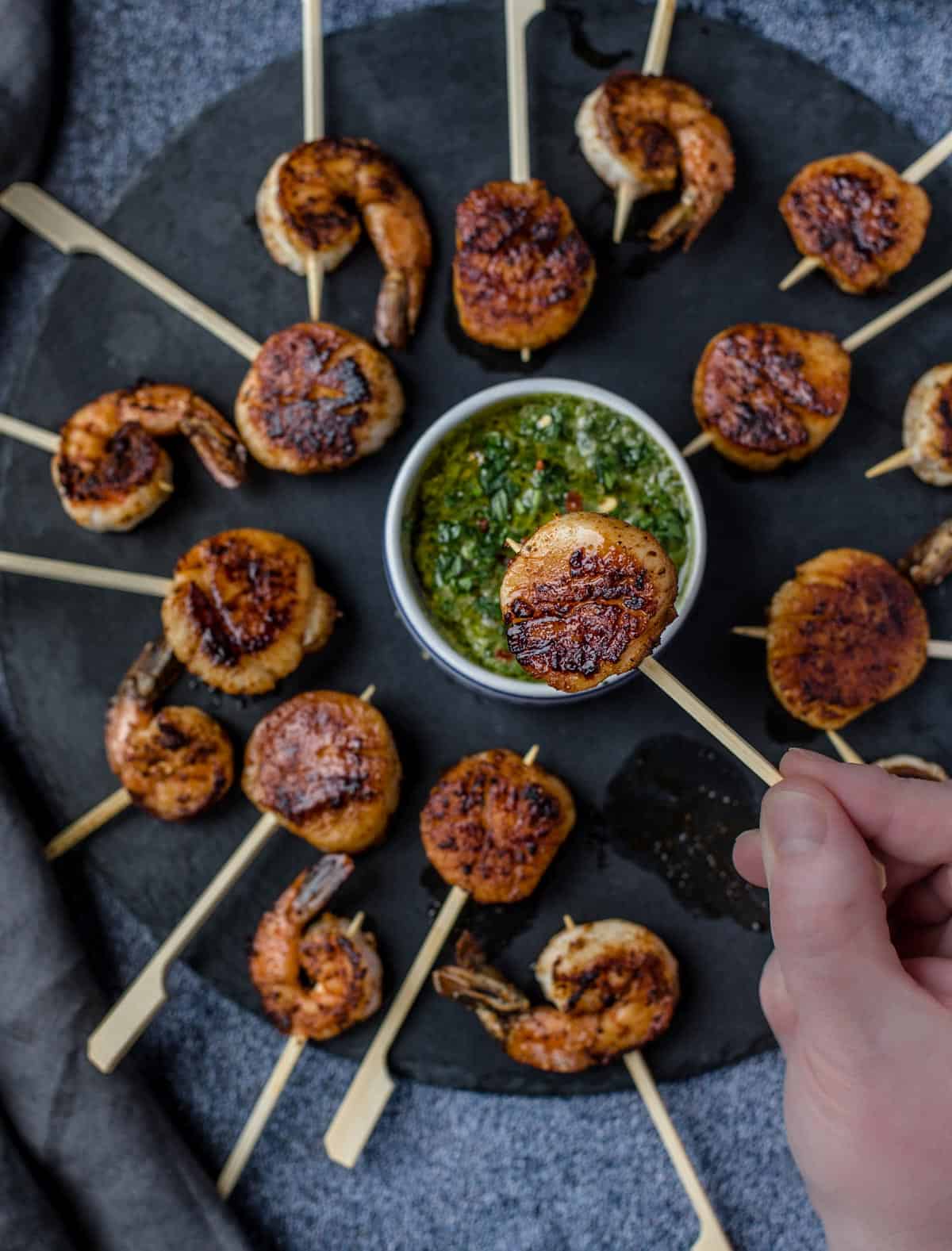 A grilled scalp on a skewer with a platter full of grilled shrimp and scallops