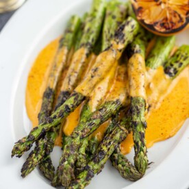 Grilled asparagus on a plate covered in BBQ hollandaise sauce.