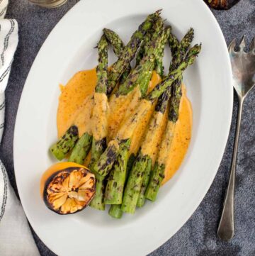 Grilled asparagus on a plate covered in hollandaise sauce.