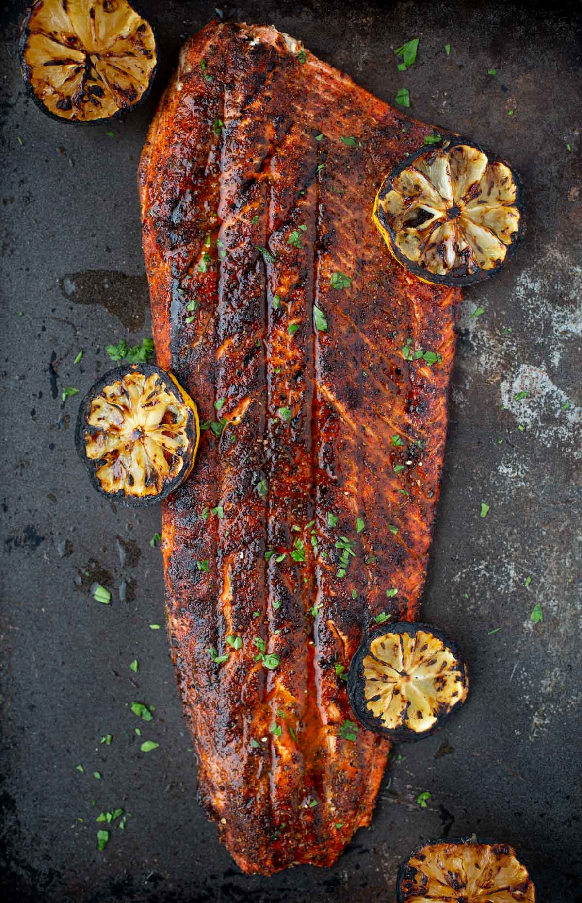 A grilled salmon whole fillet with blackened seasoning on a sheet pan with grilled lemons 