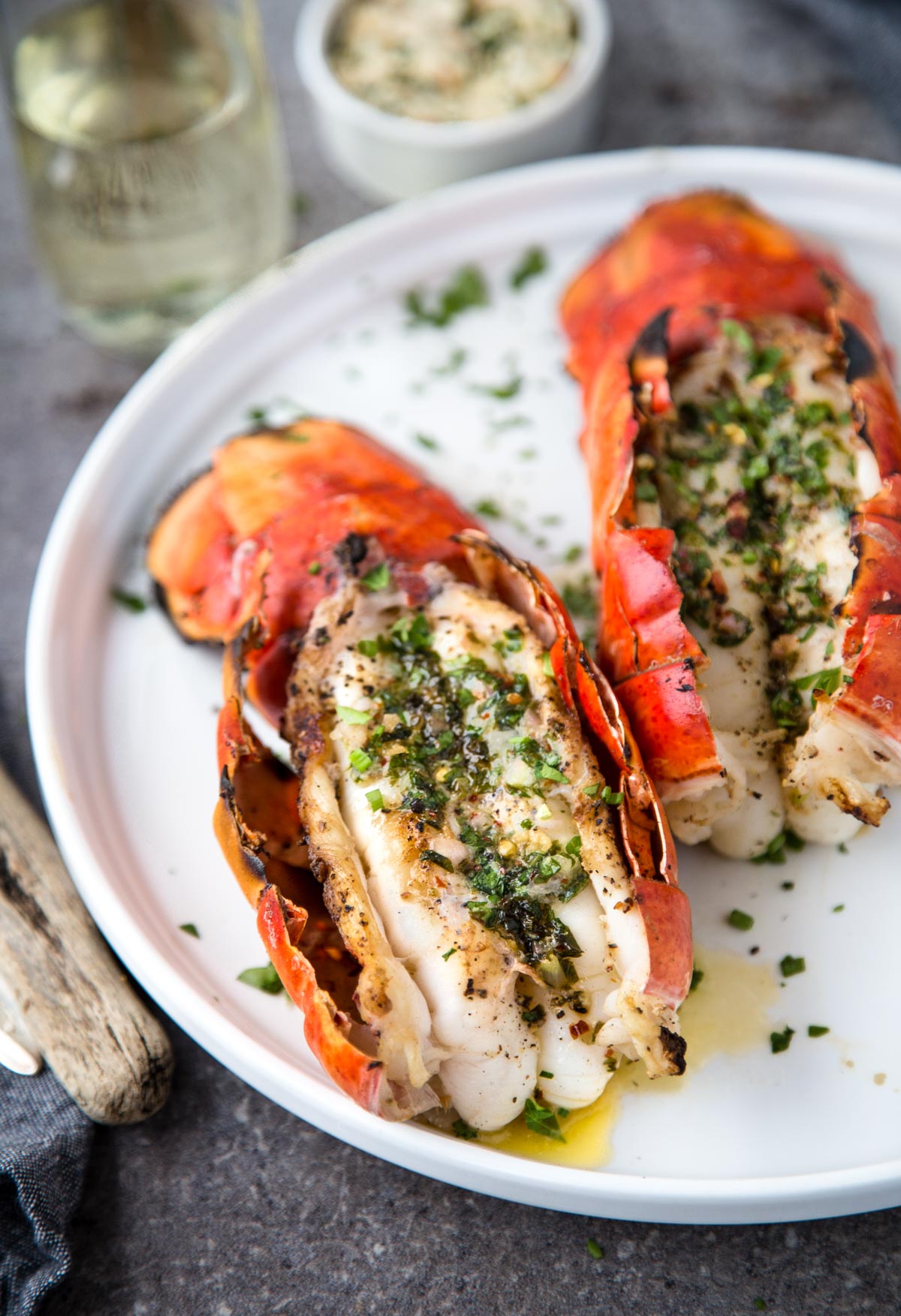 2 Grilled Lobster Tails with Herb Compound Butter on a white platter
