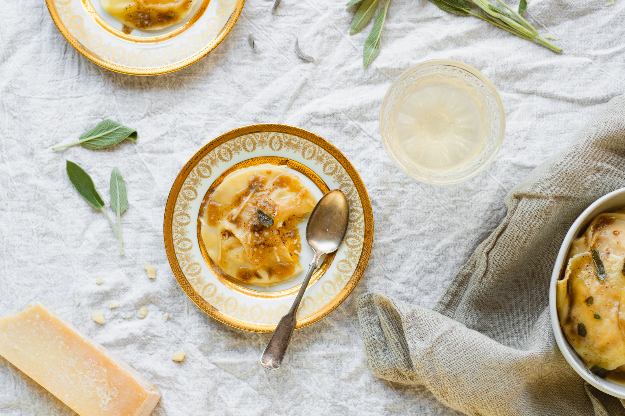 table scene of pumpkin ravioli, sage leaves, and sparkling wine