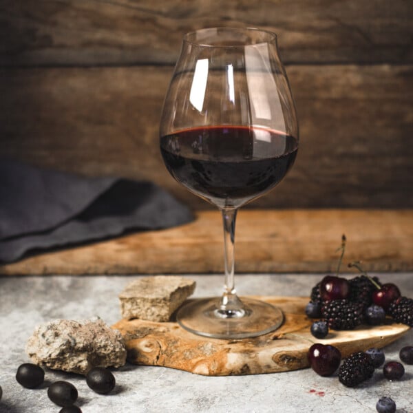 red wine in a glass surrounded by dark fruit