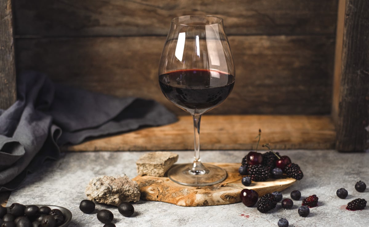 red wine in a glass surrounded by dark fruit