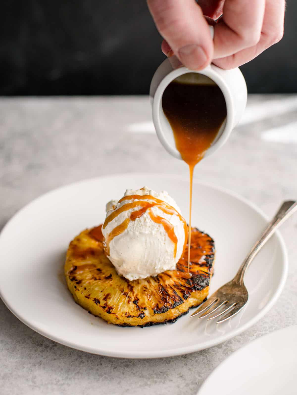 Pouring rum glaze over ice cream and grilled pineapple.