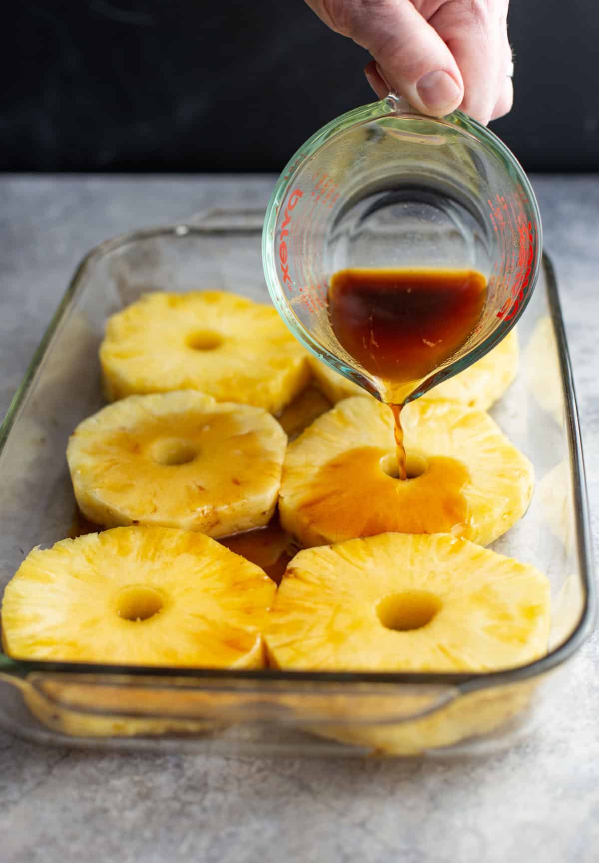 Pouring the rum soak marinade into a pan of pineapple slices.