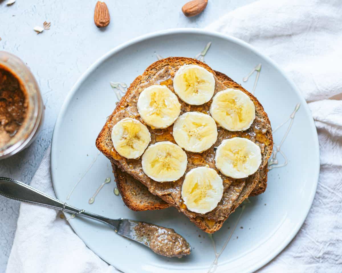 A plate with toast covered in almond butter, banana slices, and honey