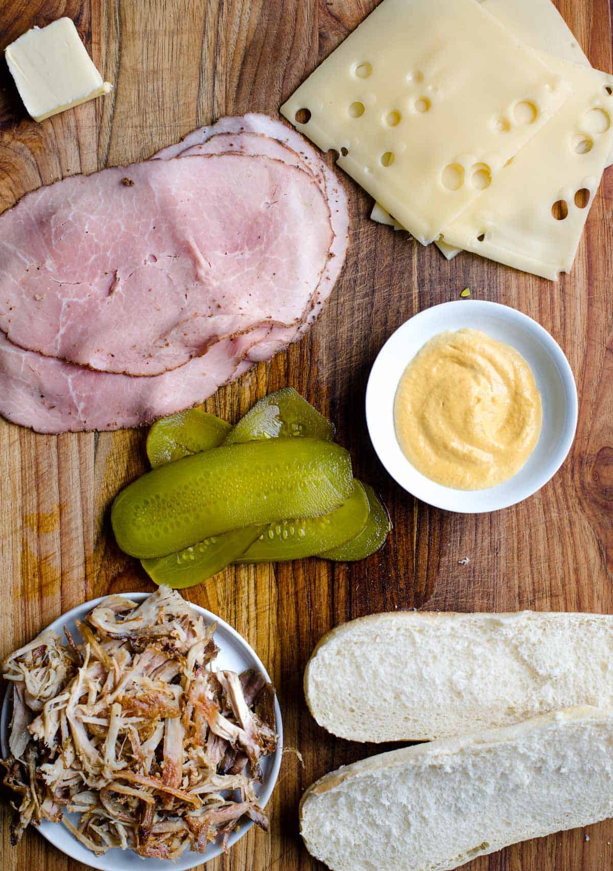 Ingredients on a cutting board for a smoked pulled pork Cuban sandwich recipe.