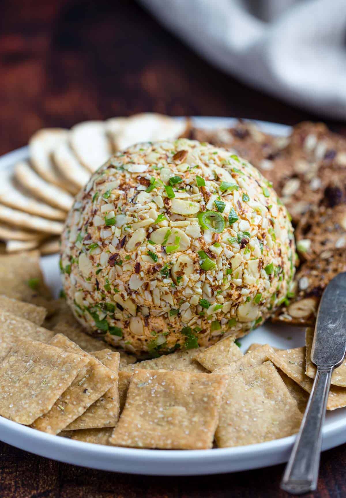 A smoked cheeseball coated with smoked almonds on a platter with crackers