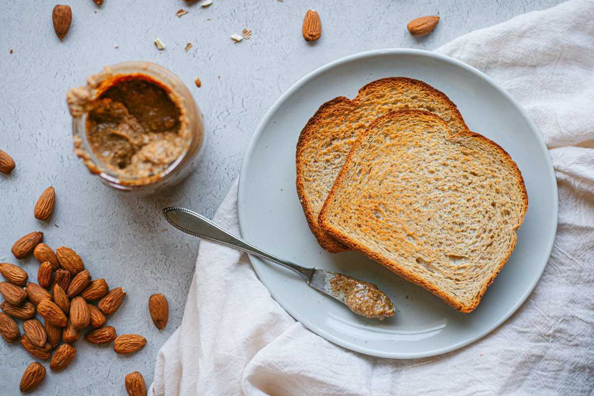 A plate with dry toast, almond, and and jar of almond butter