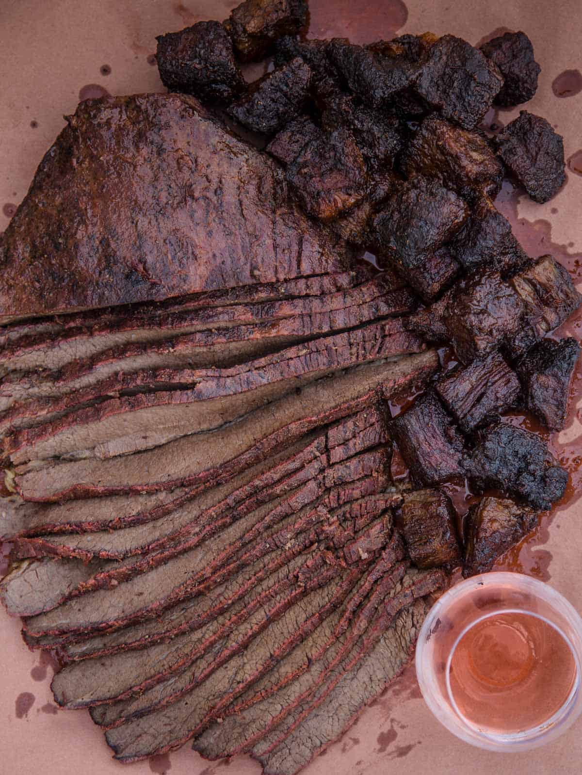 Slices of brisket flat and cubes of BBQ Burnt Ends on a serving dish with a glass of wine