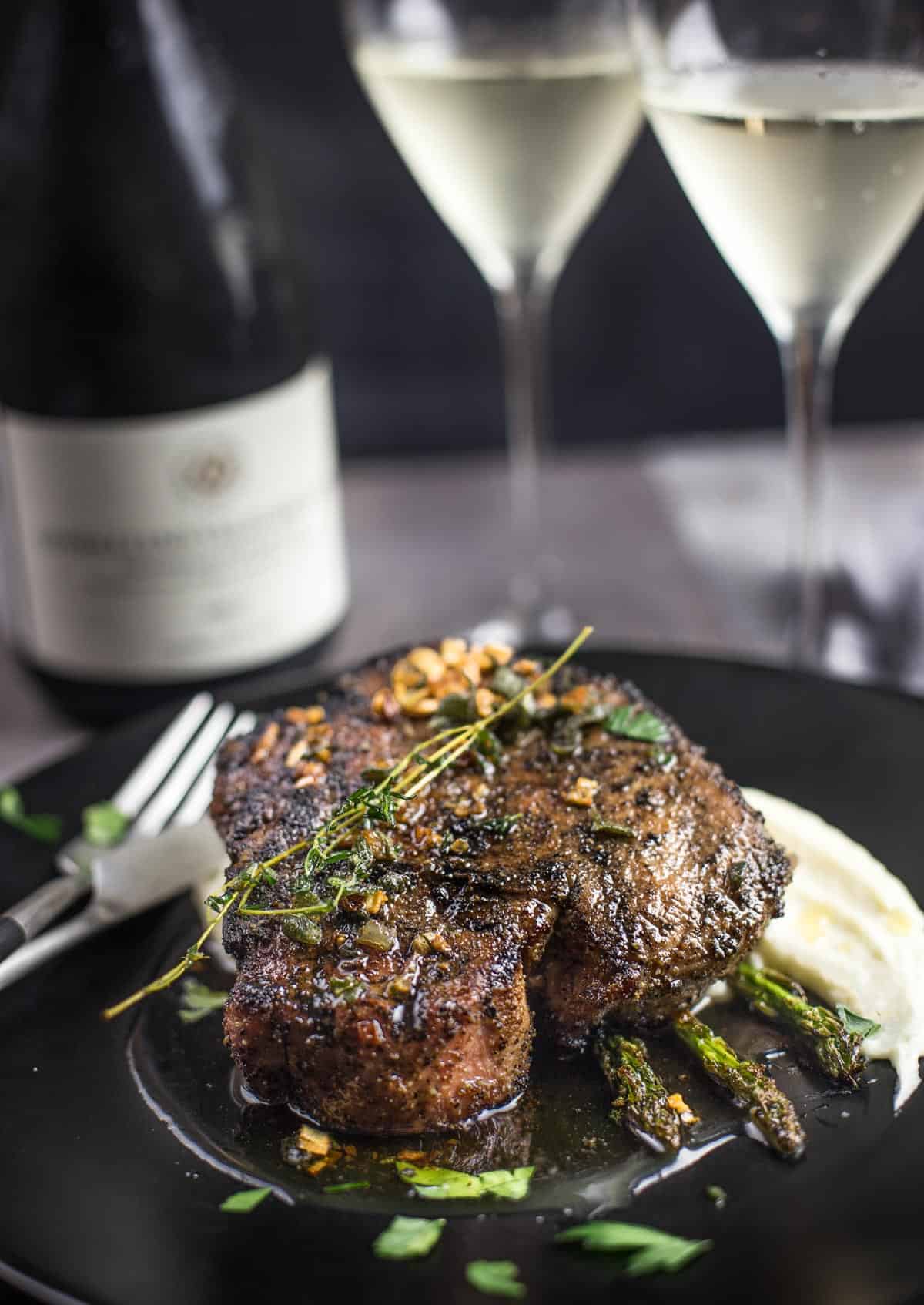 A grilled pork chop topped with a wine brown butter sauce on a serving plate