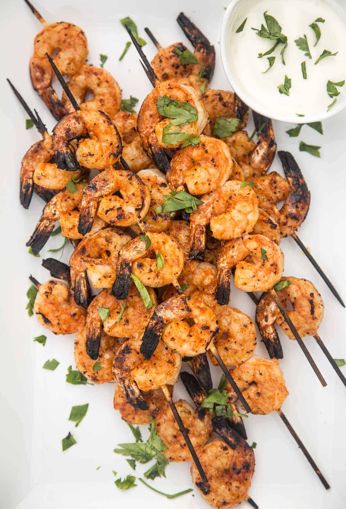 Skewers of grilled spicy shrimp on a serving dish with a dipping sauce.