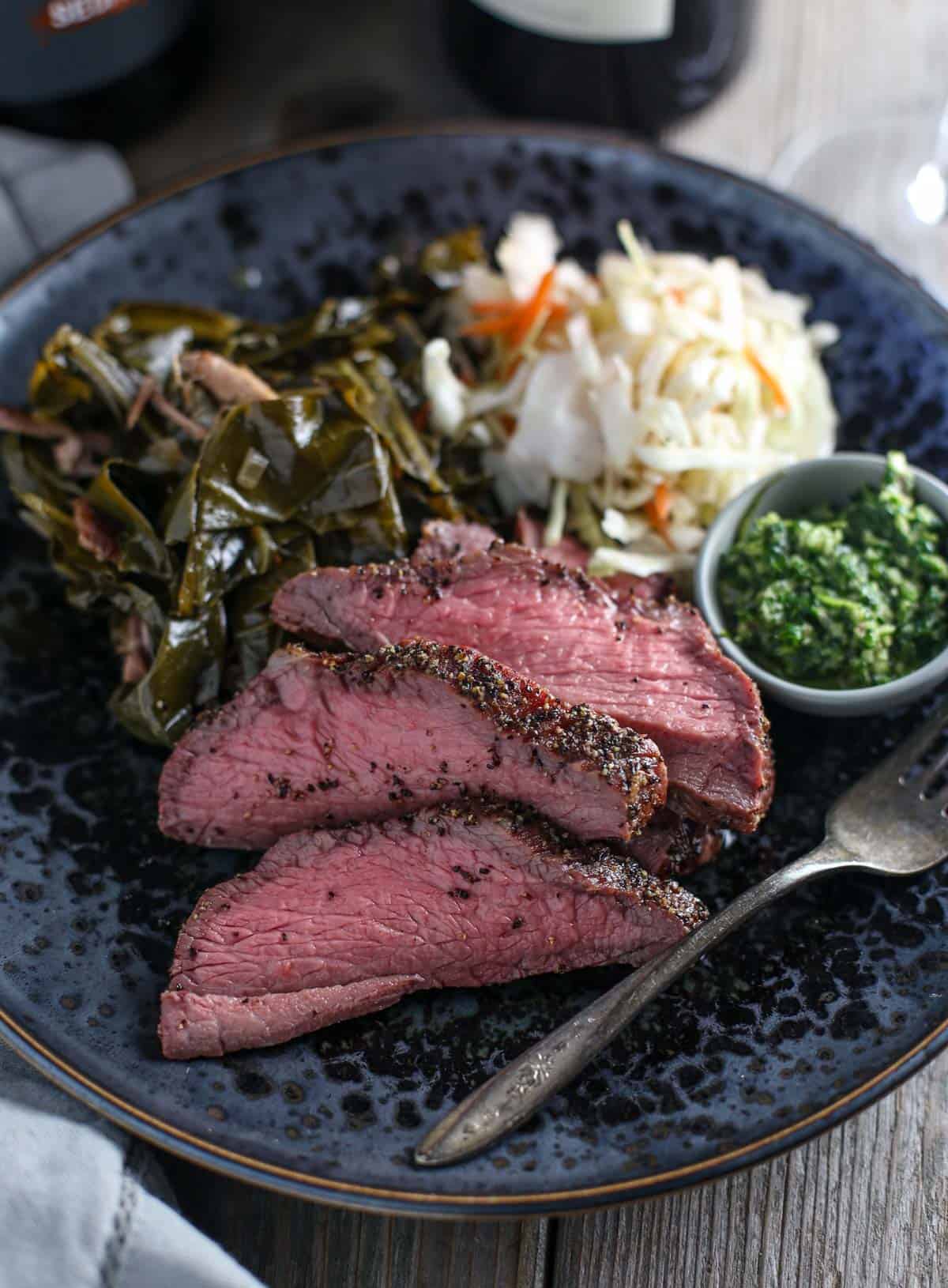 Smoked tri tip on a plate with collards and coleslaw.
