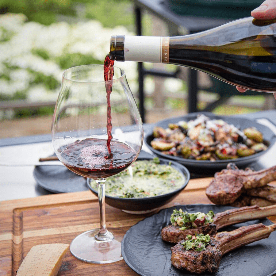 Wine from Vindulge Wine shop being poured into a glass with grilled lamb chops.