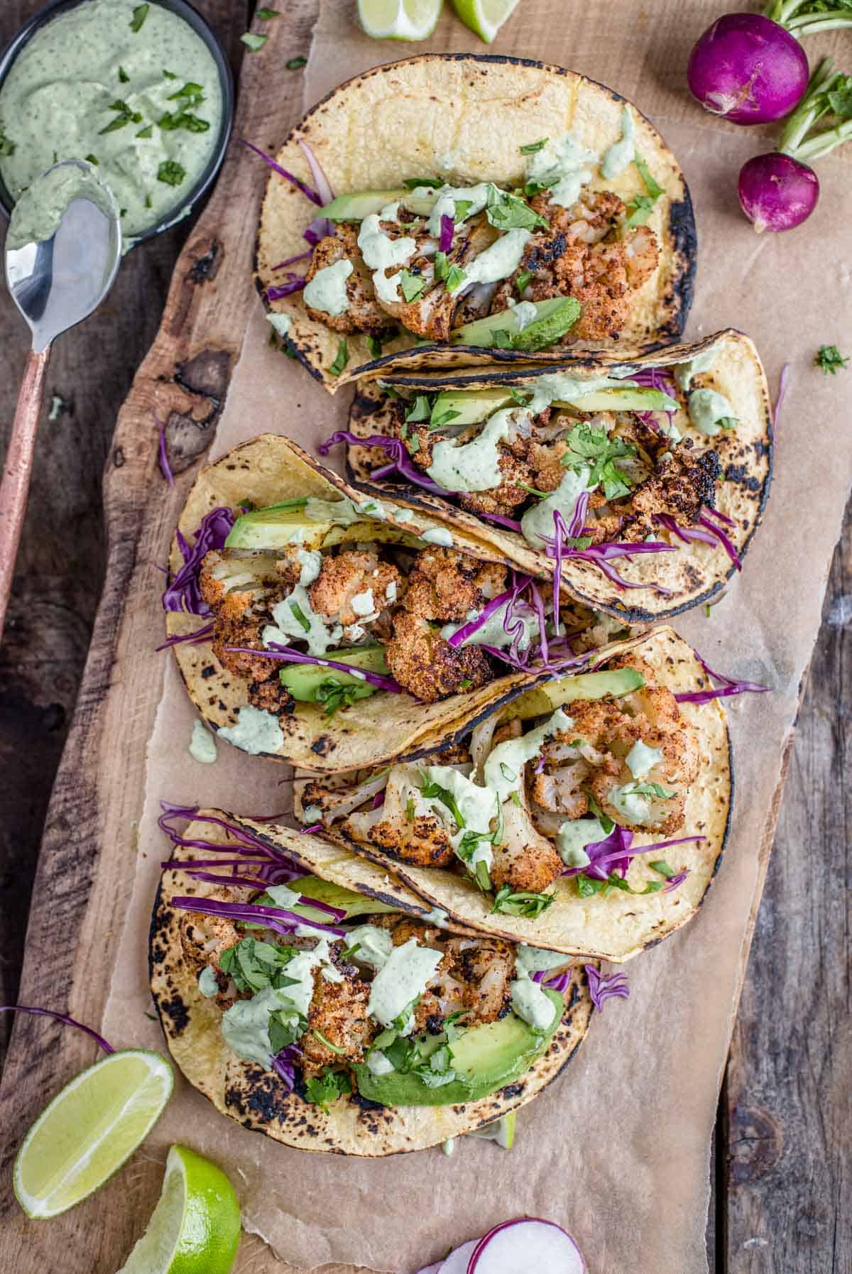 5 Grilled Cauliflower Tacos on a wood board and topped with Avocado lime cream and taco toppings.