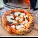 A margherita pizza on a wooden pizza peel outside a pizza oven.