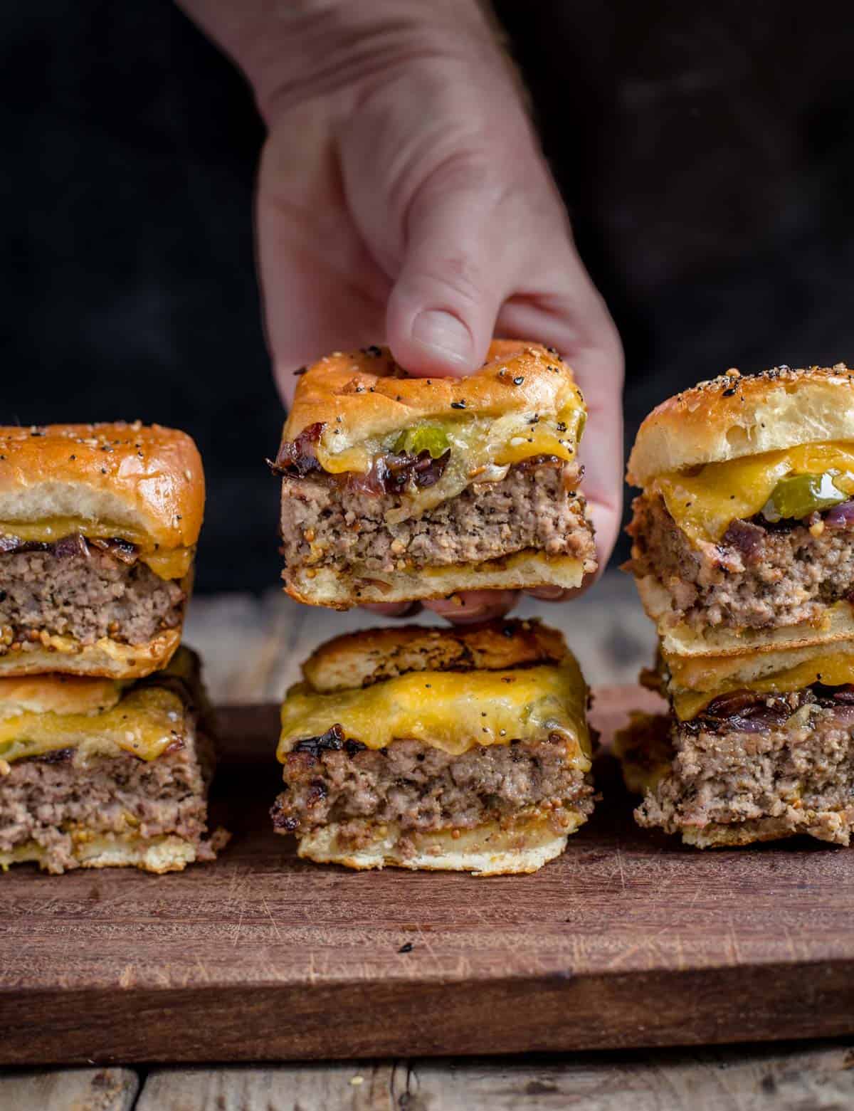 Holding one of six cheeseburger sliders on a cutting board.