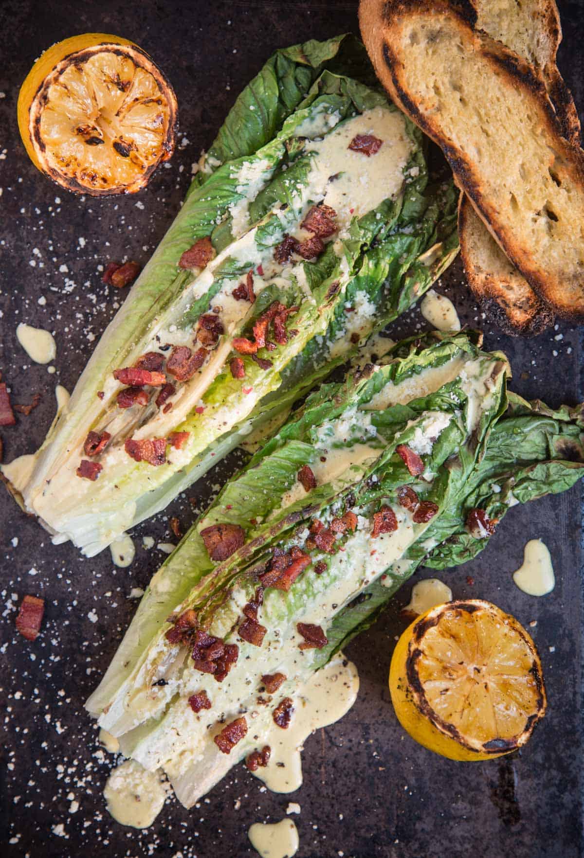 Grilled Romaine Caesar salad on a serving dish with some grilled lemon and toasted bread