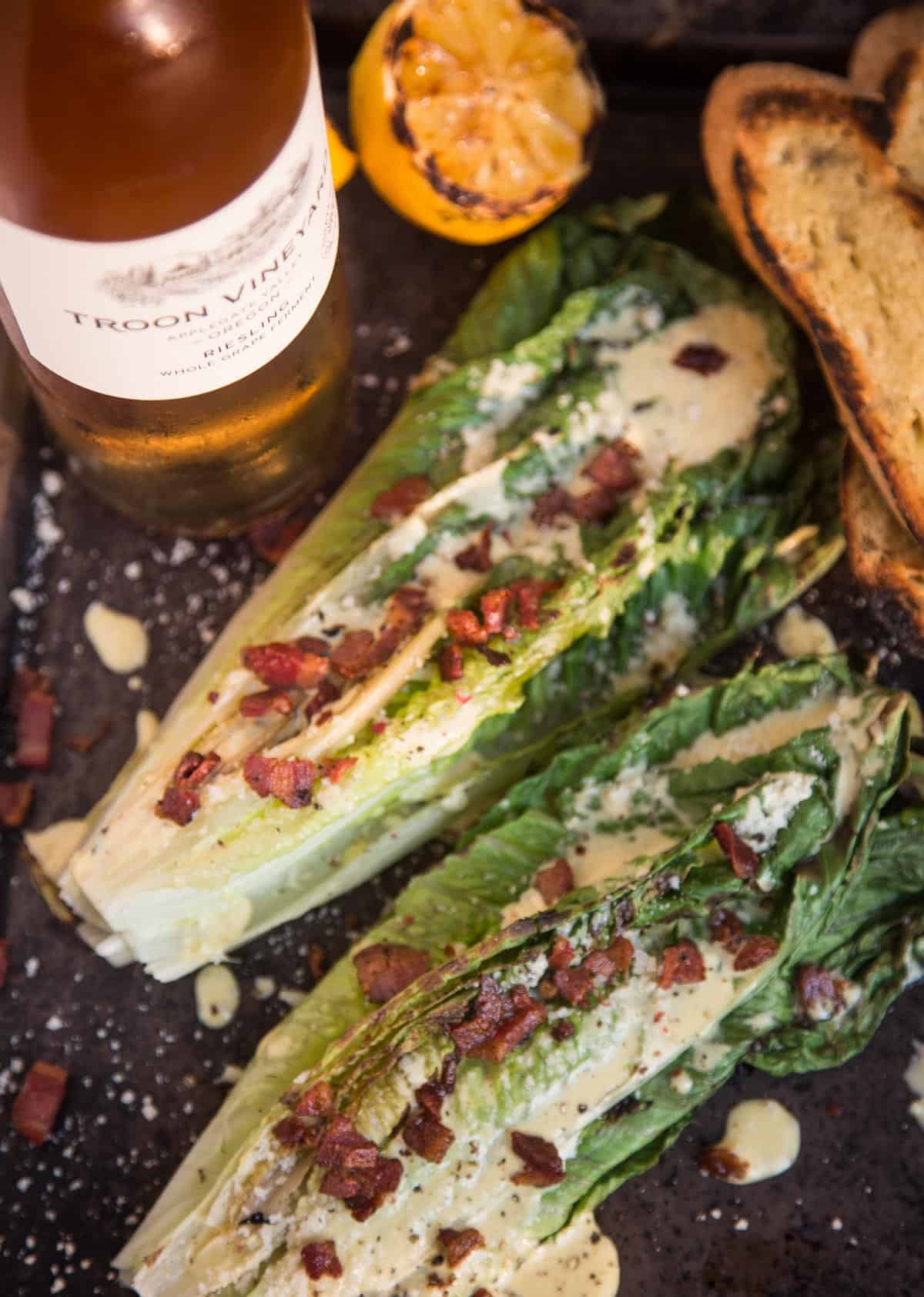 Grilled Caesar salad on a platter with a bottle of wine 