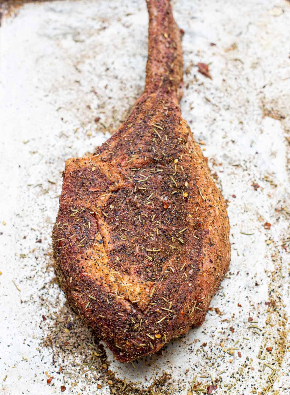 Raw tomahawk steak with herbal beef rub on it.