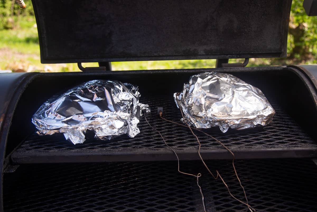 two wrapped baking dishes in a smoker