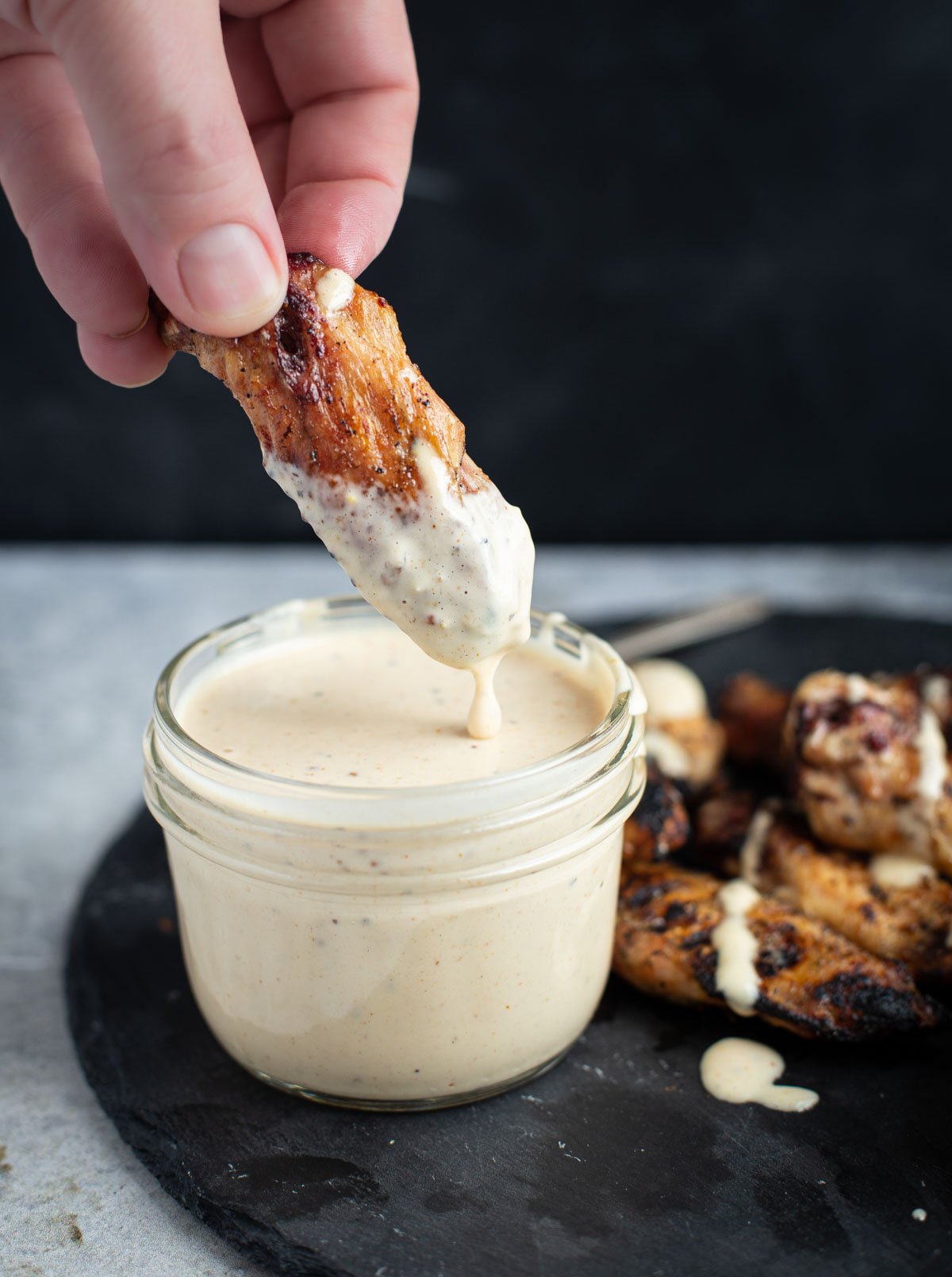 Chicken wings being dipped in Alabama White BBQ Sauce.