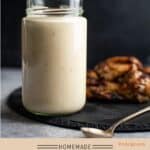 Large mason jar of Alabama white BBQ sauce with a spoon and chicken wings in the background