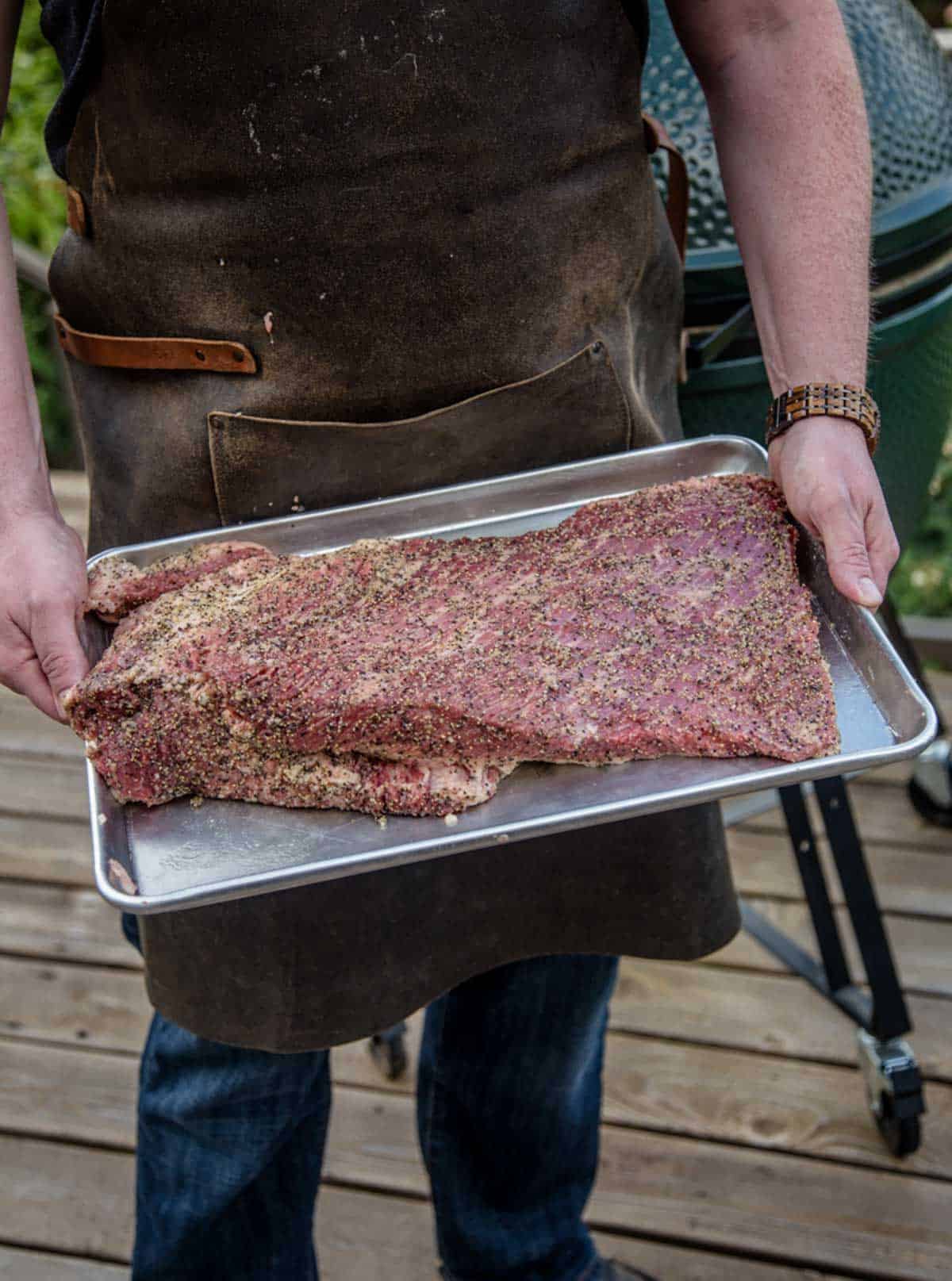 A man holding a seasoned raw brisket in a sheet pan