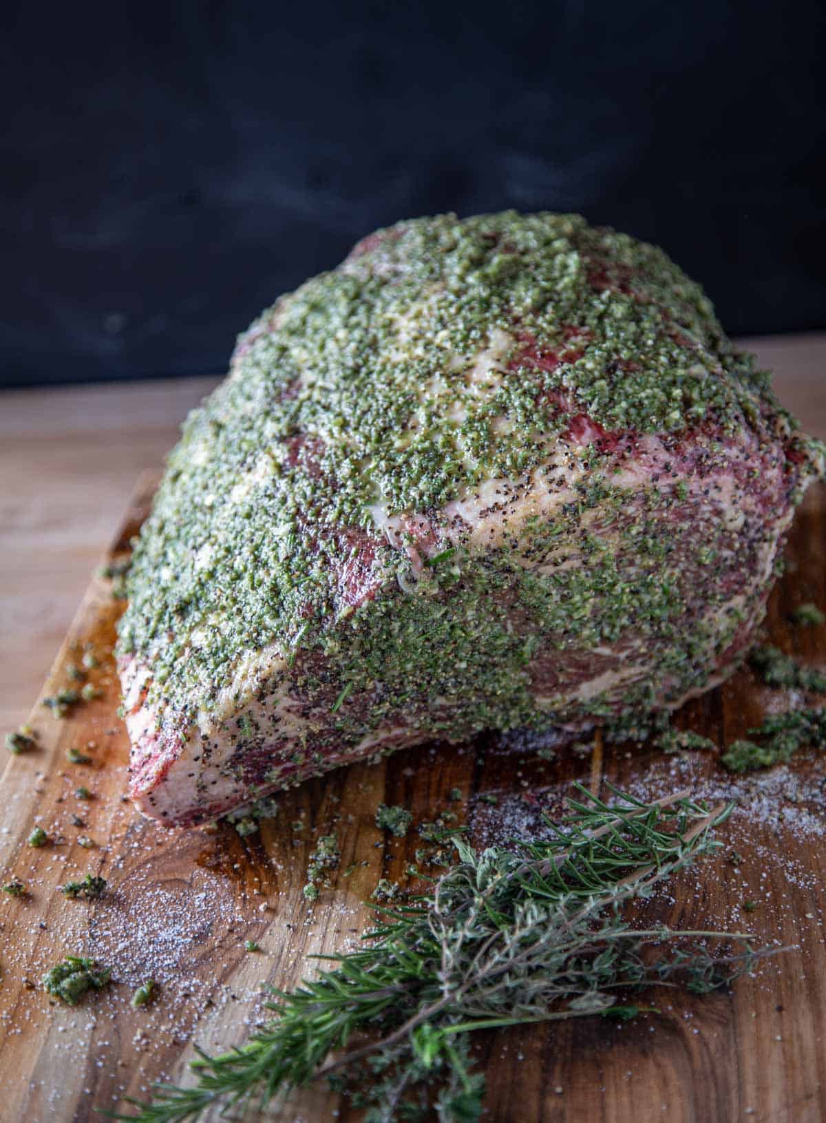 Prime Rib Roast seasoned with herb paste on a cutting board.