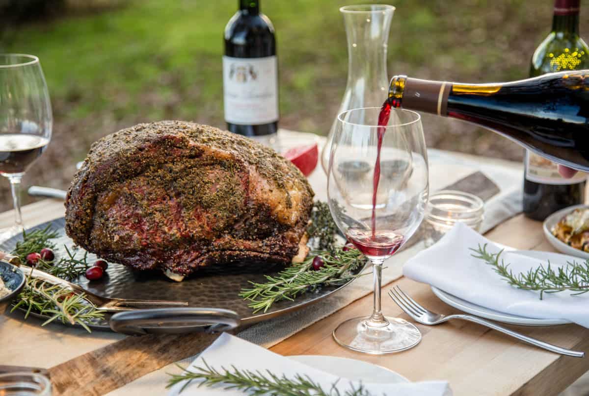 Red wine poured into a glass on table scape of holiday prime rib roast.