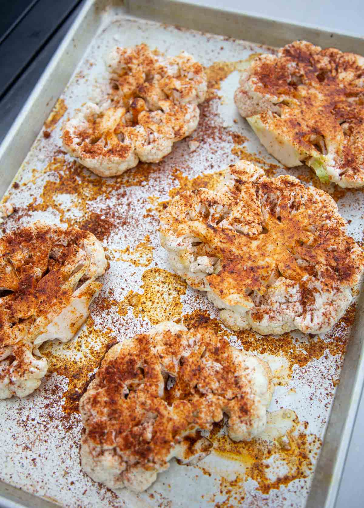 Cauliflower steaks getting seasoned on a sheet pan.