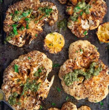 Grilled Cauliflower Steaks on a sheet pan topped with Chimichurri sauce