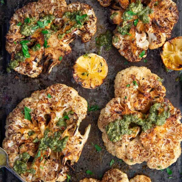 Grilled Cauliflower Steaks on a sheet pan topped with Chimichurri sauce