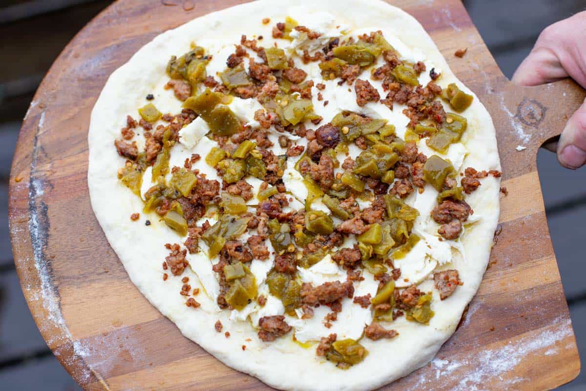 Green chile pizza toppings on dough before going in the oven.