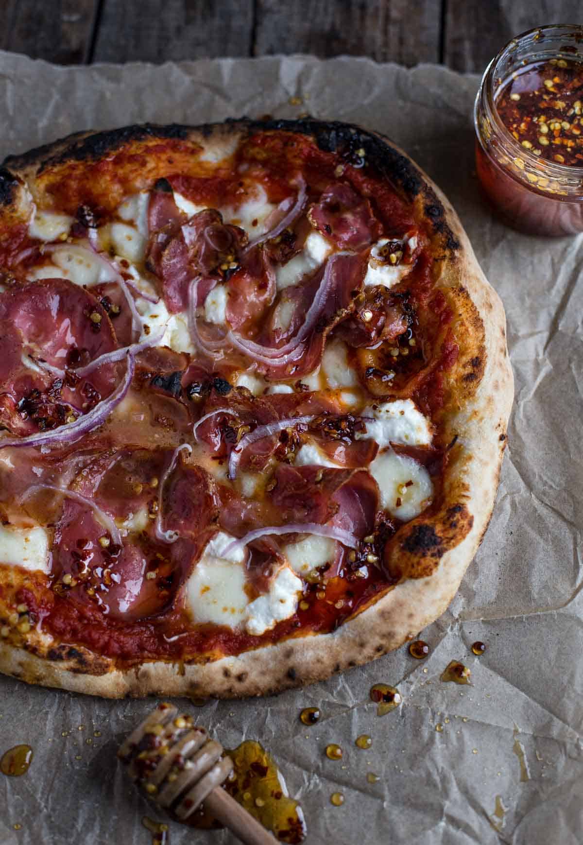 Hot Honey Pizza with prosciutto and ricotta on a serving dish with hot honey in a mason jar on the side