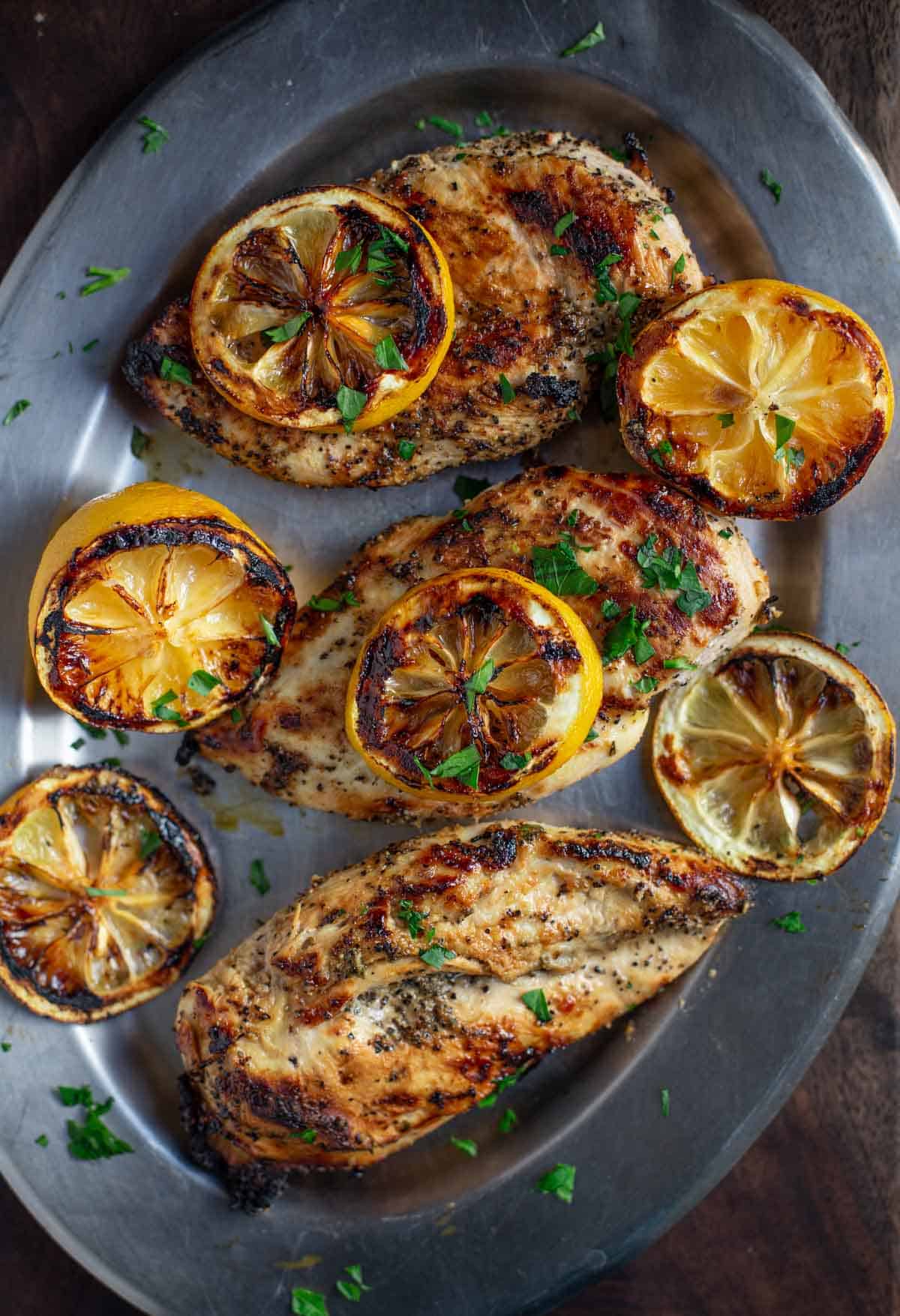 Grilled lemon pepper chicken breast on a platter with grilled lemon.
