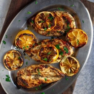 Grilled lemon pepper chicken on platter with grilled lemon.