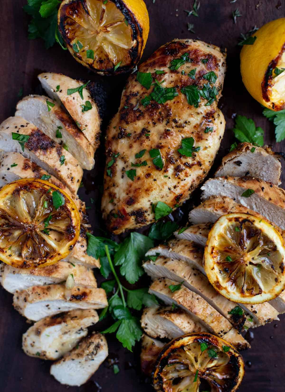 Slices of grilled lemon pepper chicken and grilled lemon garnish.