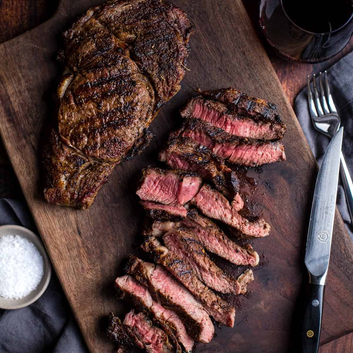 Two grilled ribeye steaks on a cutting board