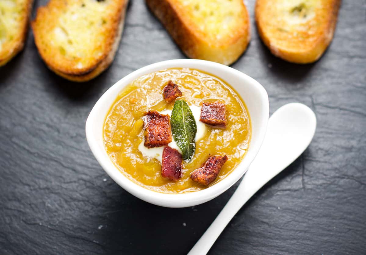 A cup of smoked butternut squash soup topped with smoked bacon and sage