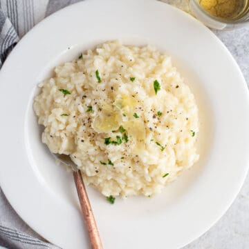 Prosecco risotto in a bowl with shaved Parmesan cheese, a spoon, and fresh parsley.