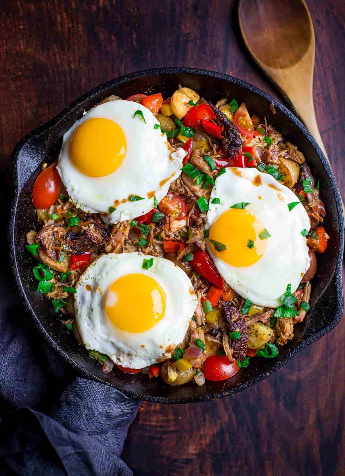 Pulled pork breakfast hash in cast iron pan with eggs over the top.