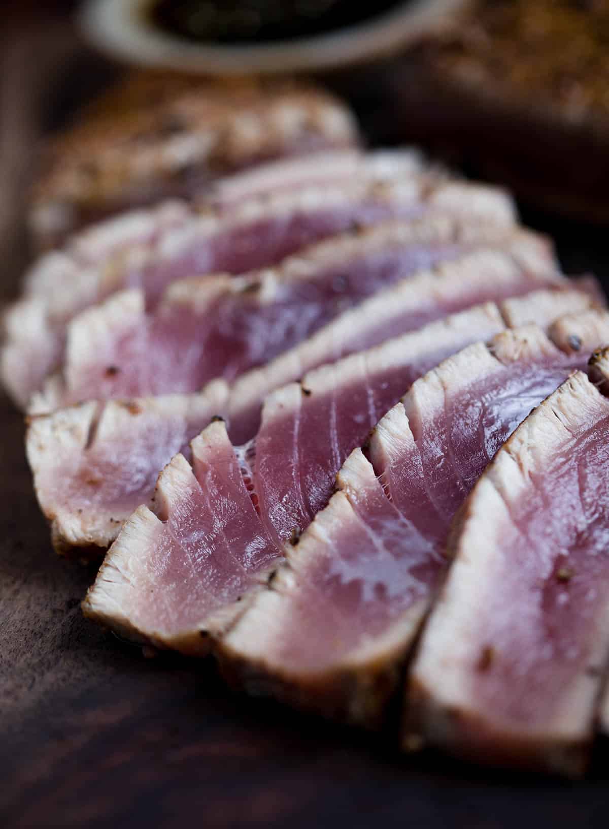 Slices of grilled ahi tuna steaks on a cutting board with dipping sauce.