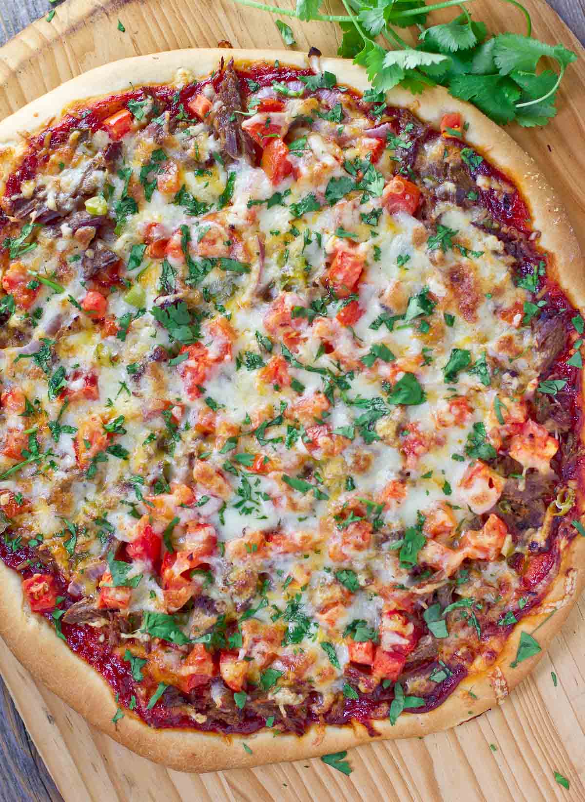 Brisket pizza unsliced on a cutting board.