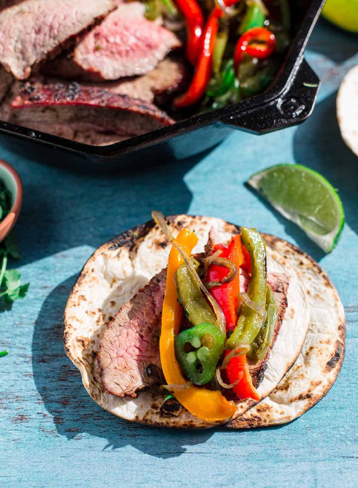Tri Tip fajitas with sides and toppings on a wearing board.