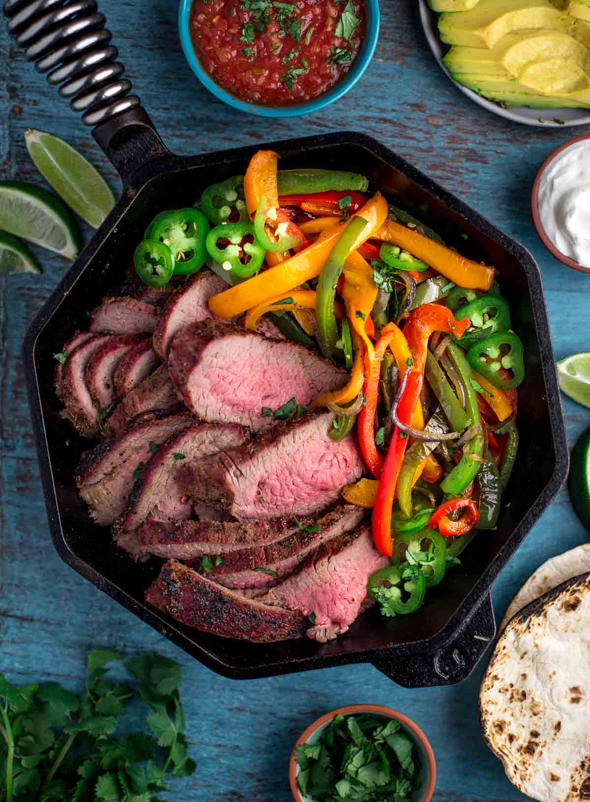 Tri tip slices with onions and peppers in a skillet for fajitas.
