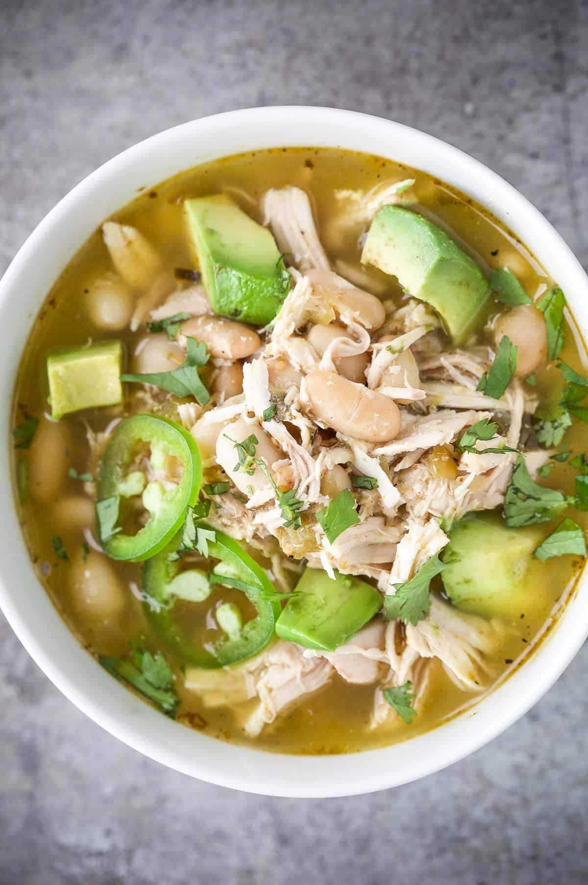 A bowl of smoked verde chicken soup topped with avocado and jalapeño slices